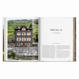 Calimia Home Great Escapes Alps book open to the Brücke 49 spread showing a historic stone guesthouse in Vals.