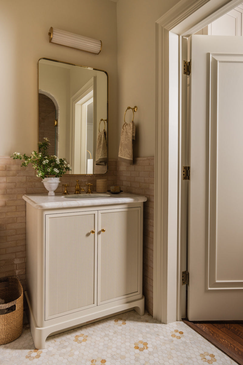 Bathroom with a fluted cream vanity, hex mosaic floor, and a brass-framed mirror