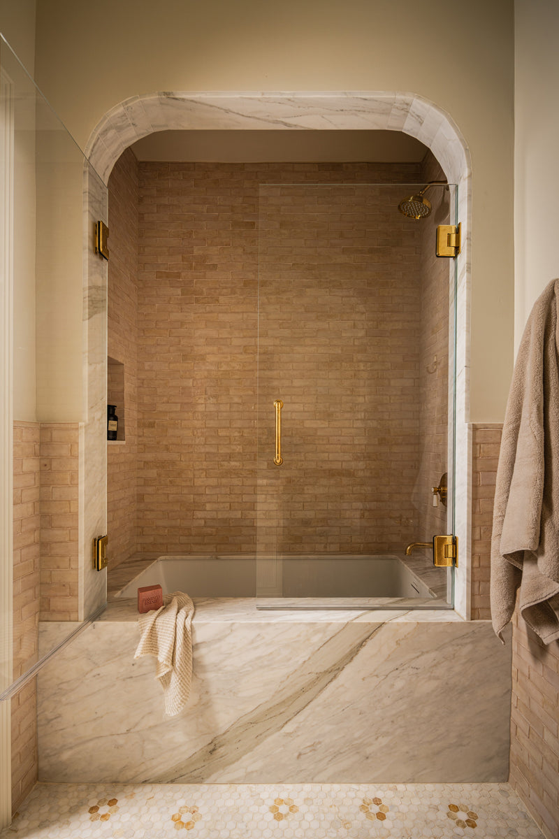 Bathroom with an arched marble shower, brass fixtures, and a plaster-toned tile surround