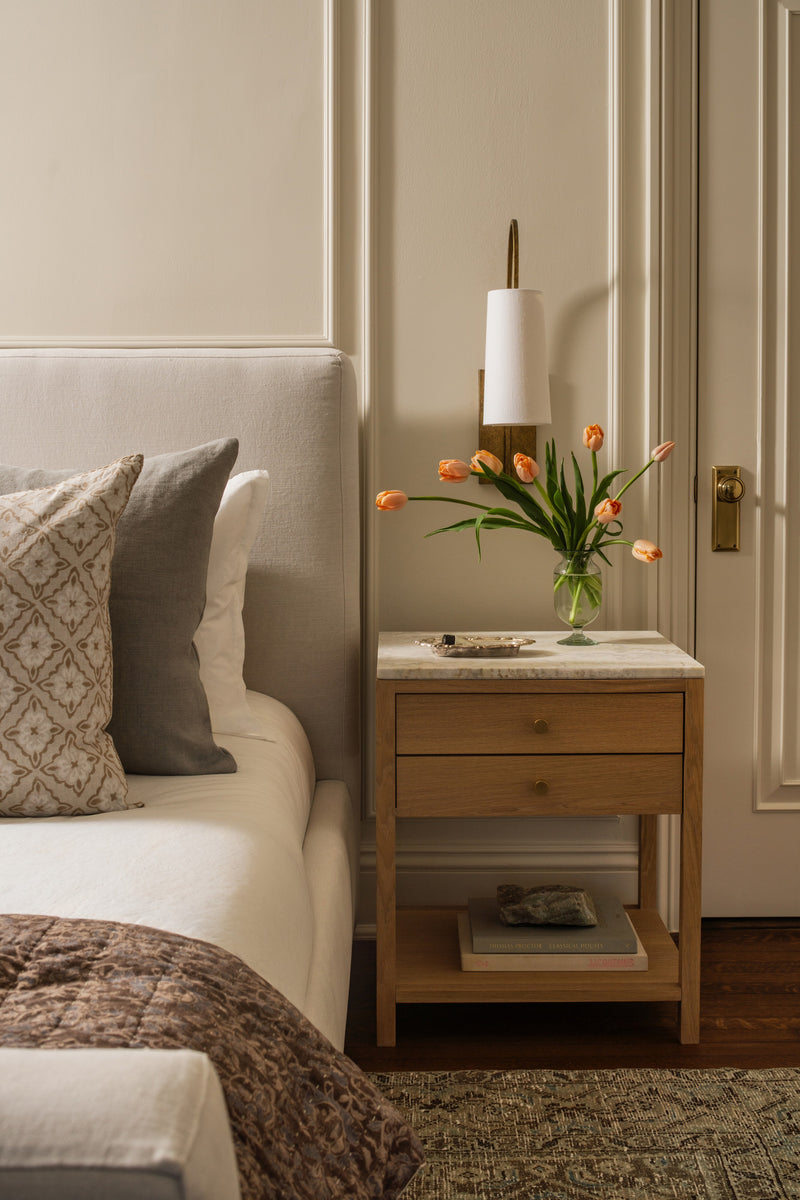 Bedroom nightstand with orange tulips, a brass sconce, and an upholstered headboard
