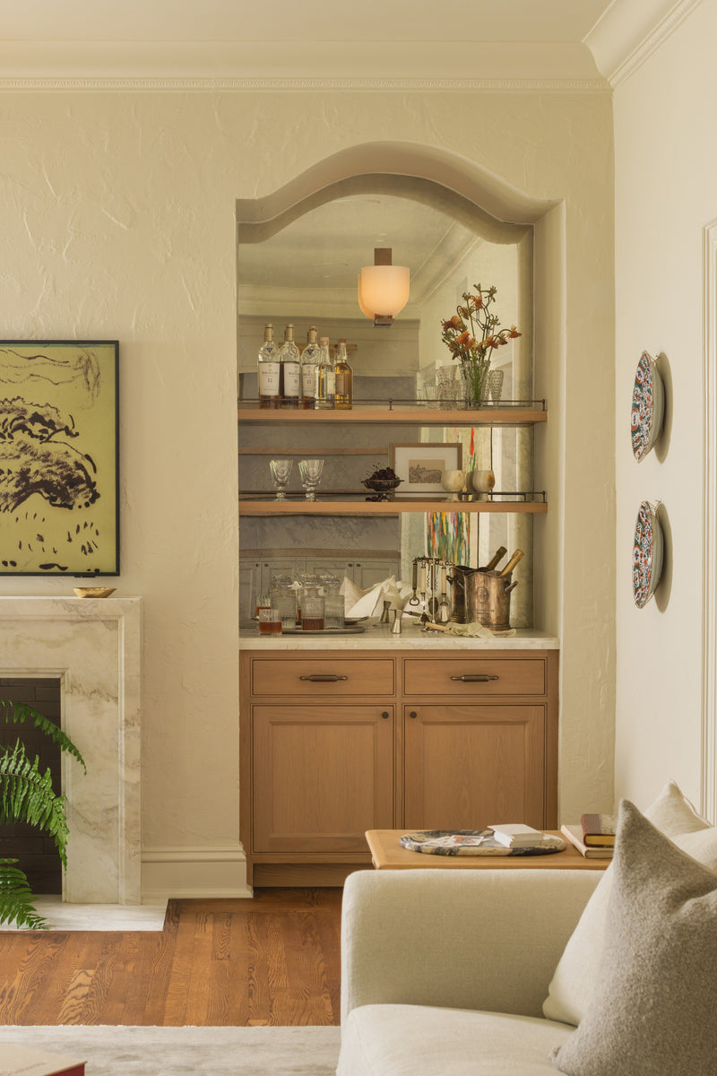Built-in bar with an arched antique mirror, oak cabinetry, and open shelves of glassware