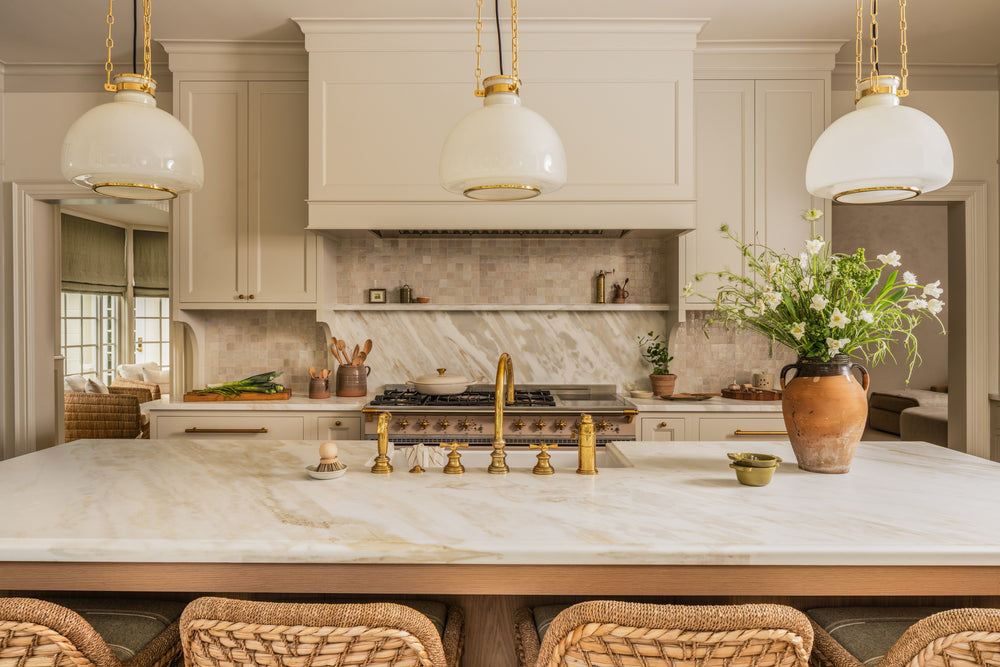 Cream kitchen with a marble-topped island, brass bridge faucet, and dome pendants