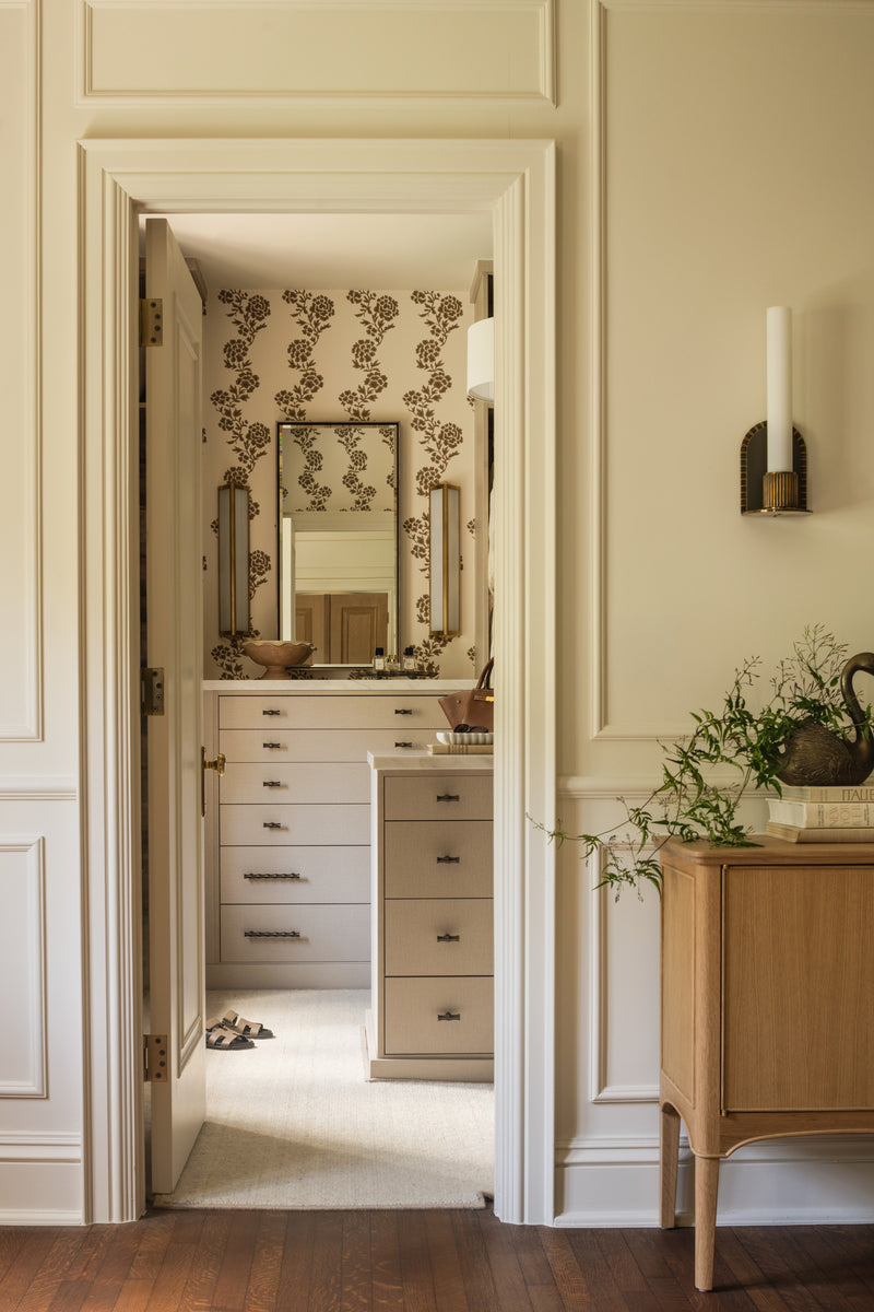 Dressing room with floral wallpaper, built-in drawers, and a niche styled with a lamp and greenery
