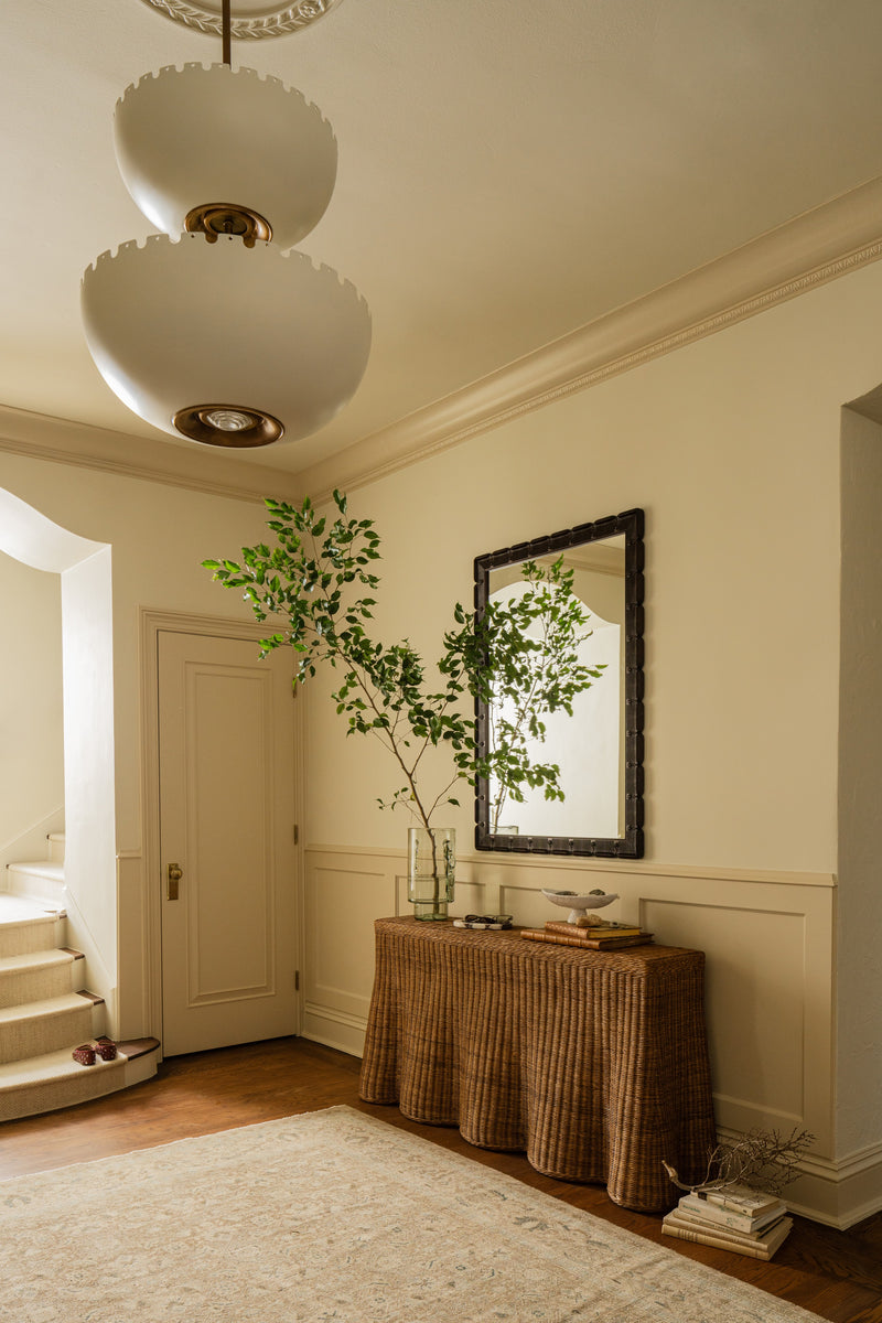 Entryway with a skirted rattan console, black-framed mirror, and potted tree against pale yellow walls