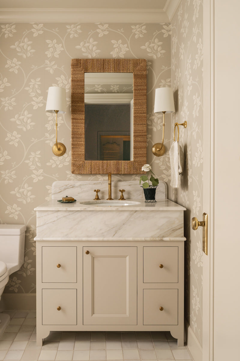Guest bathroom with a cream vanity, rattan-framed mirror, and botanical wallpaper