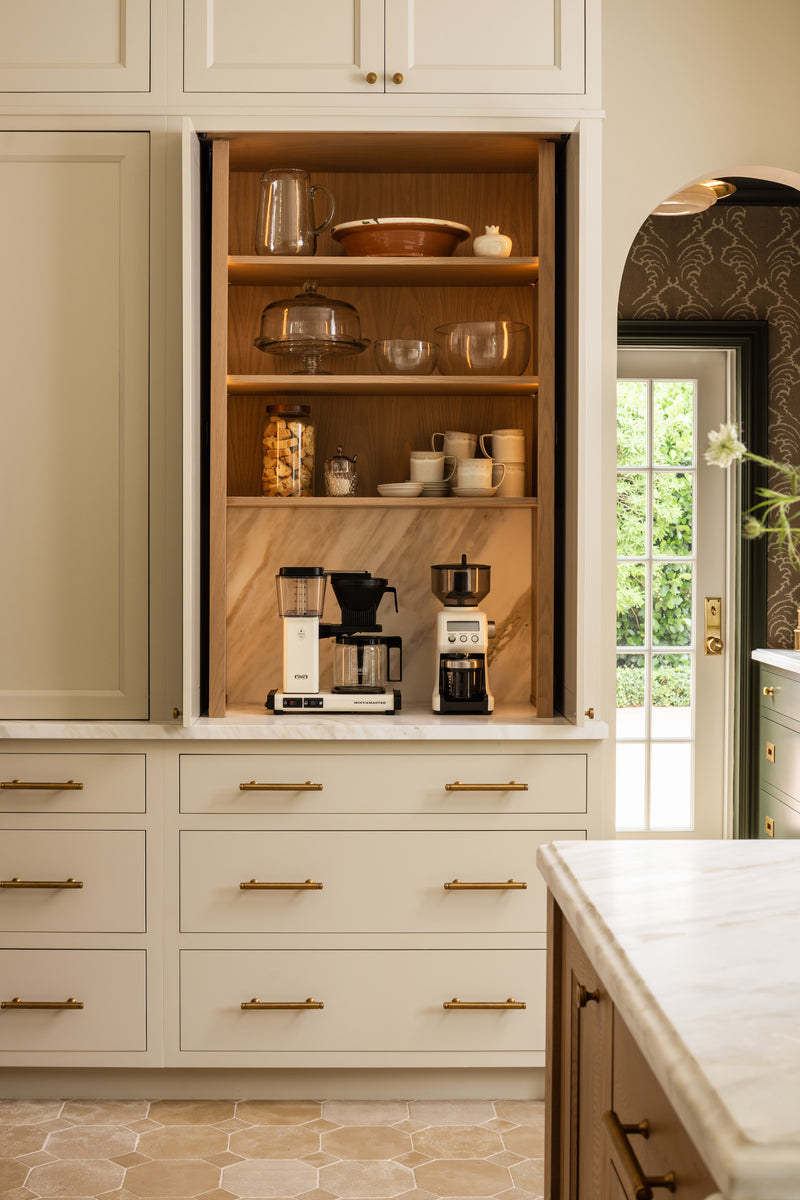 Hidden coffee bar concealed behind cabinet doors with a walnut interior and brass hardware
