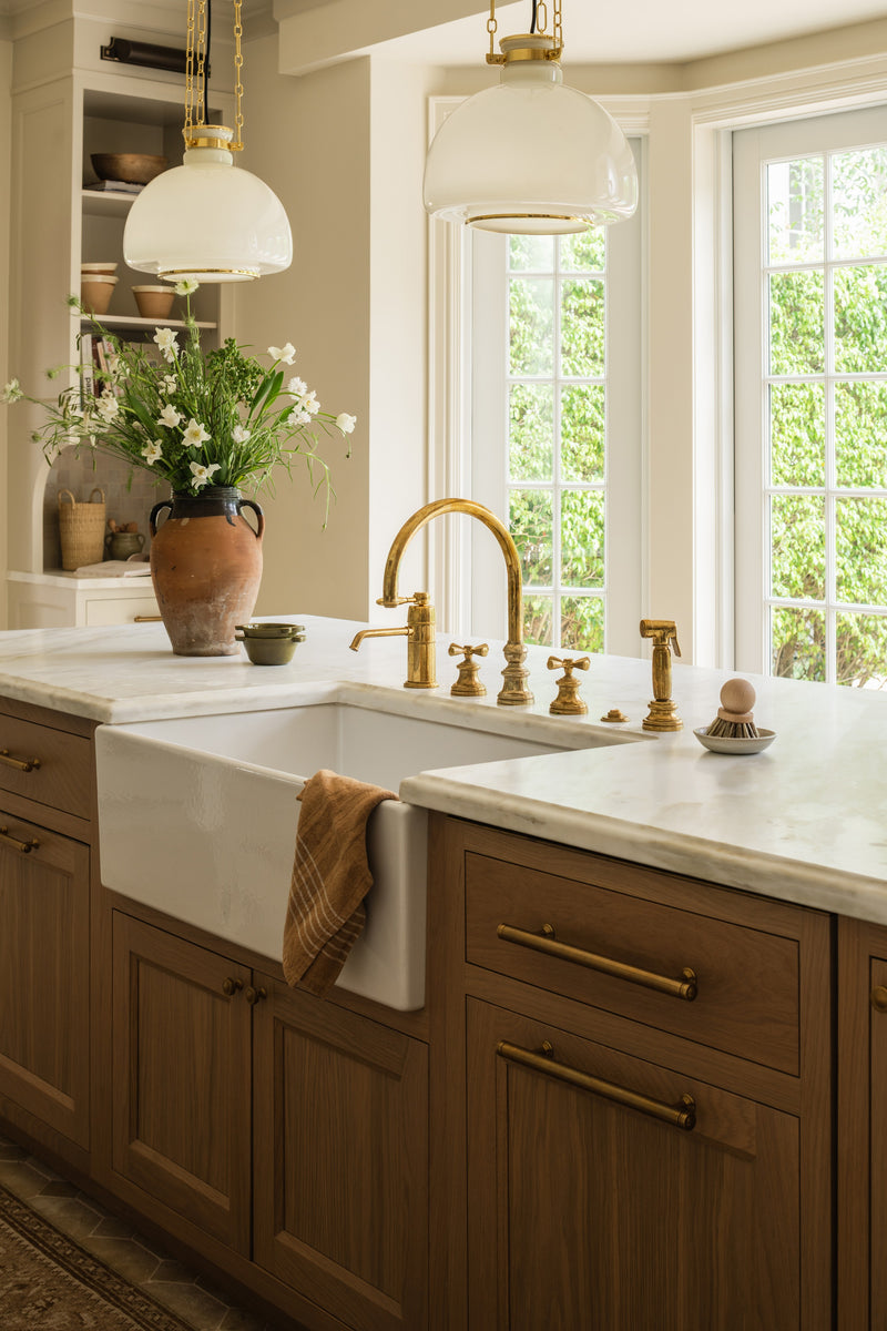 Kitchen island detail with a farmhouse sink, brass gooseneck faucet, and a terracotta vase of greenery
