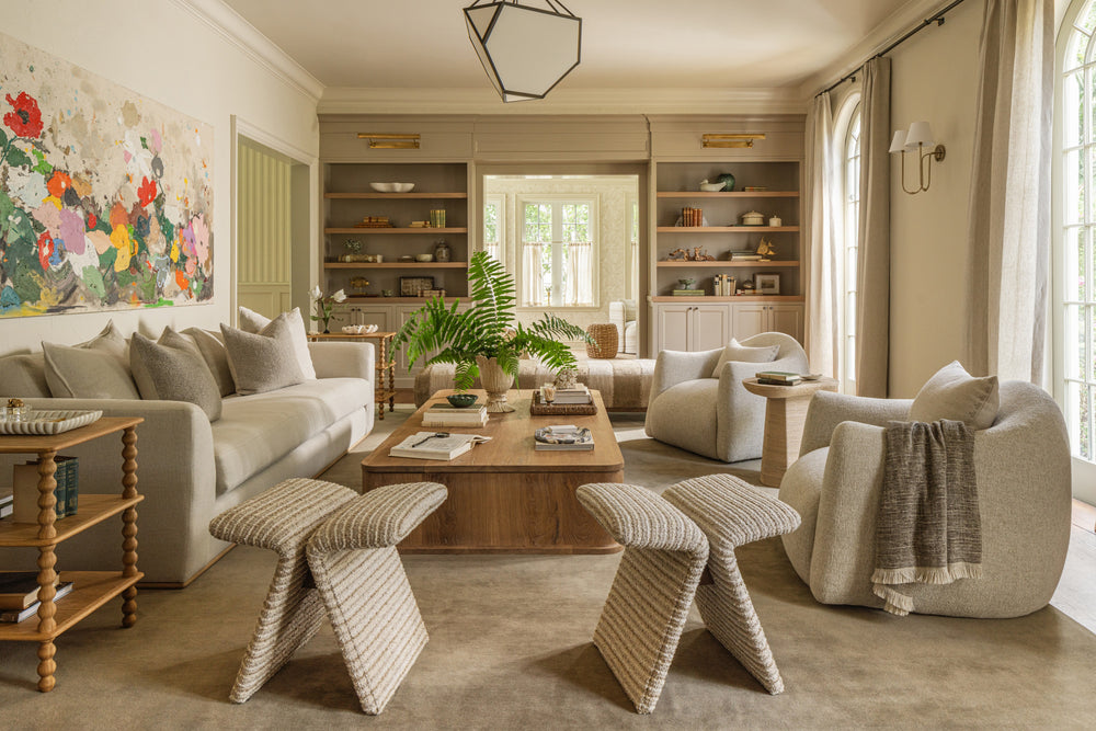 Living room with cream sofas, woven stools, built-in shelving, and a large abstract floral painting