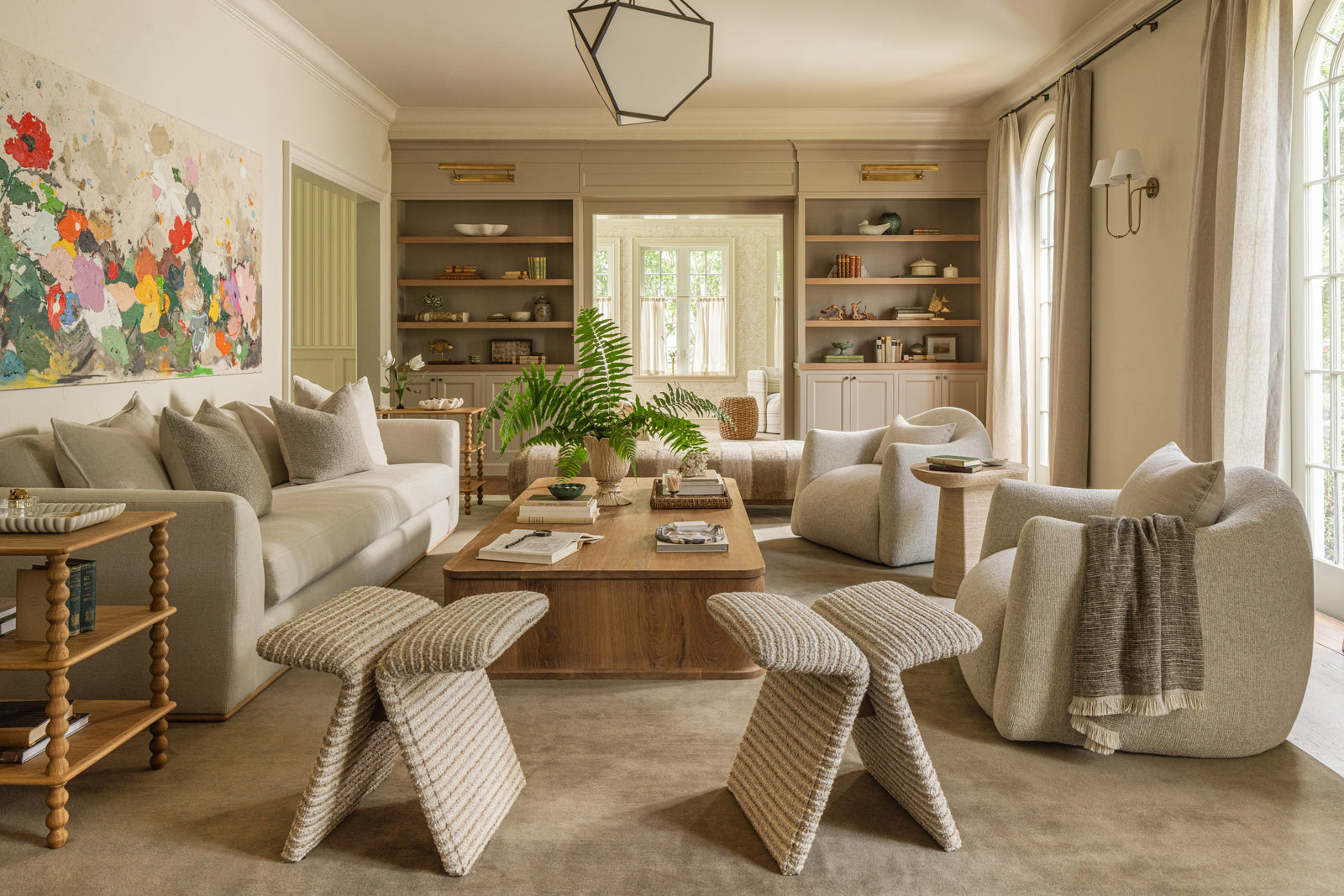 Living room with cream sofas, woven stools, built-in shelving, and a large abstract floral painting