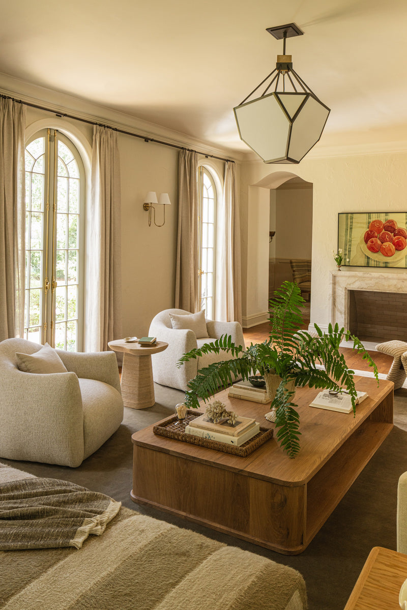 Living room with bouclé swivel chairs, a walnut coffee table, and arched windows beside the marble fireplace