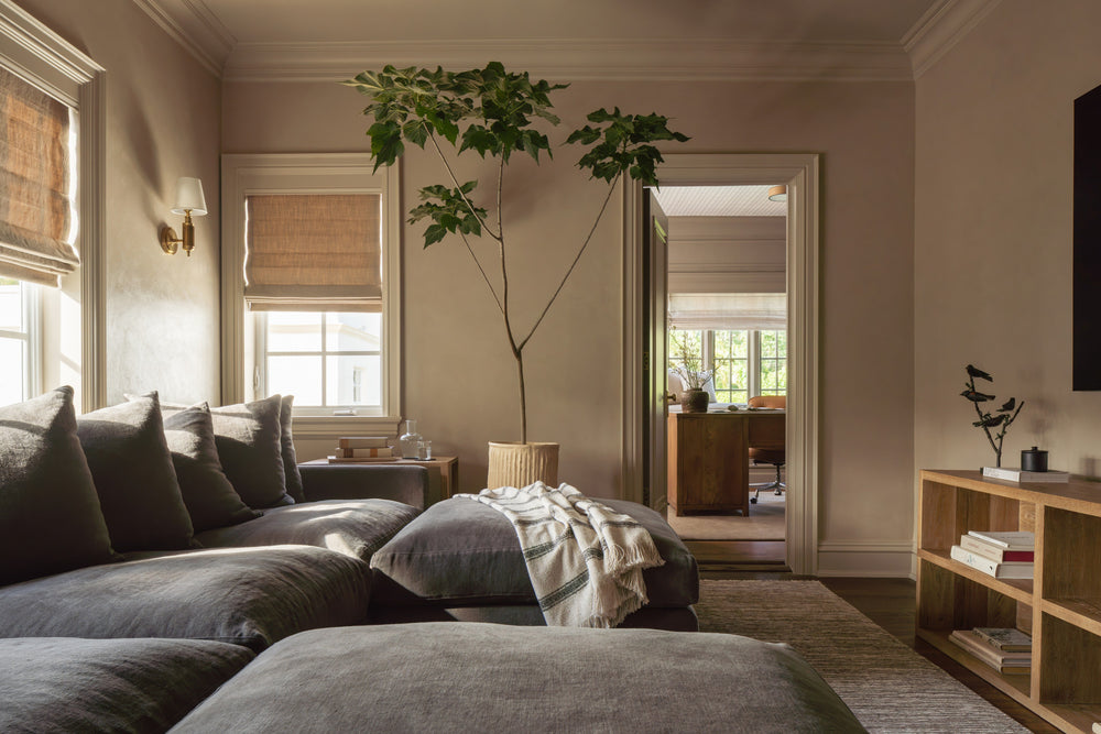 Media room with a deep gray sectional, woven shades, and a view through to the office