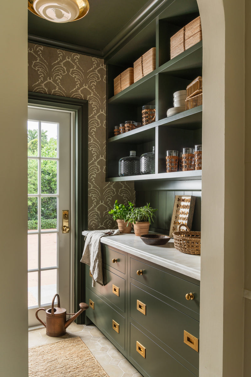 Walk-in pantry with green cabinets, damask wallpaper, and open shelving of glass storage jars