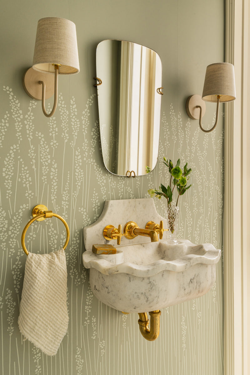 Powder room with green botanical wallpaper, a scalloped marble wall-mount sink, and brass fittings