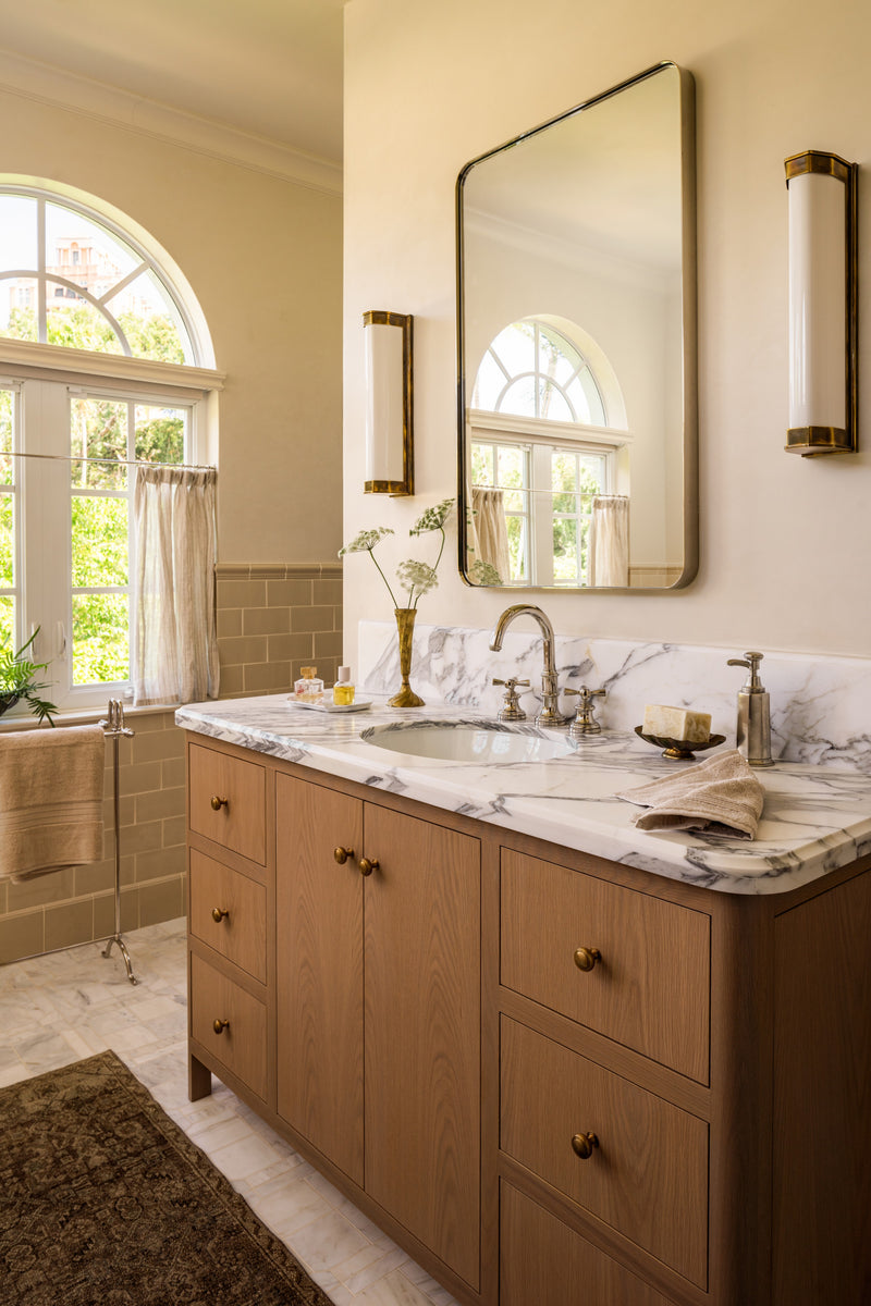 Primary bathroom with an oak double vanity, Arabescato marble counter, and an arched window