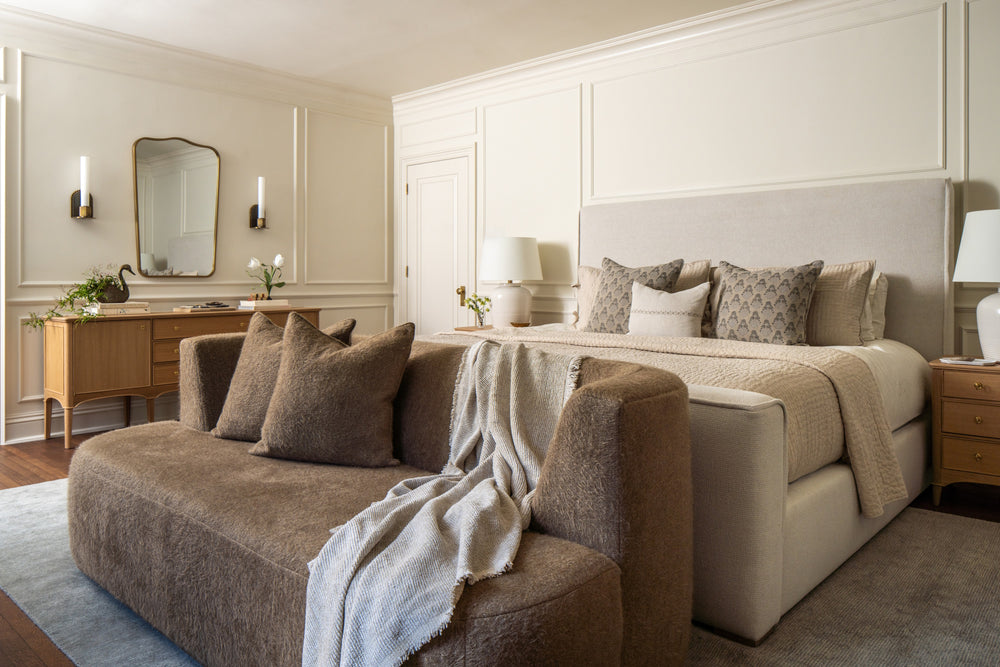 Primary bedroom with an upholstered bed, mohair settee, and wall molding in soft neutrals