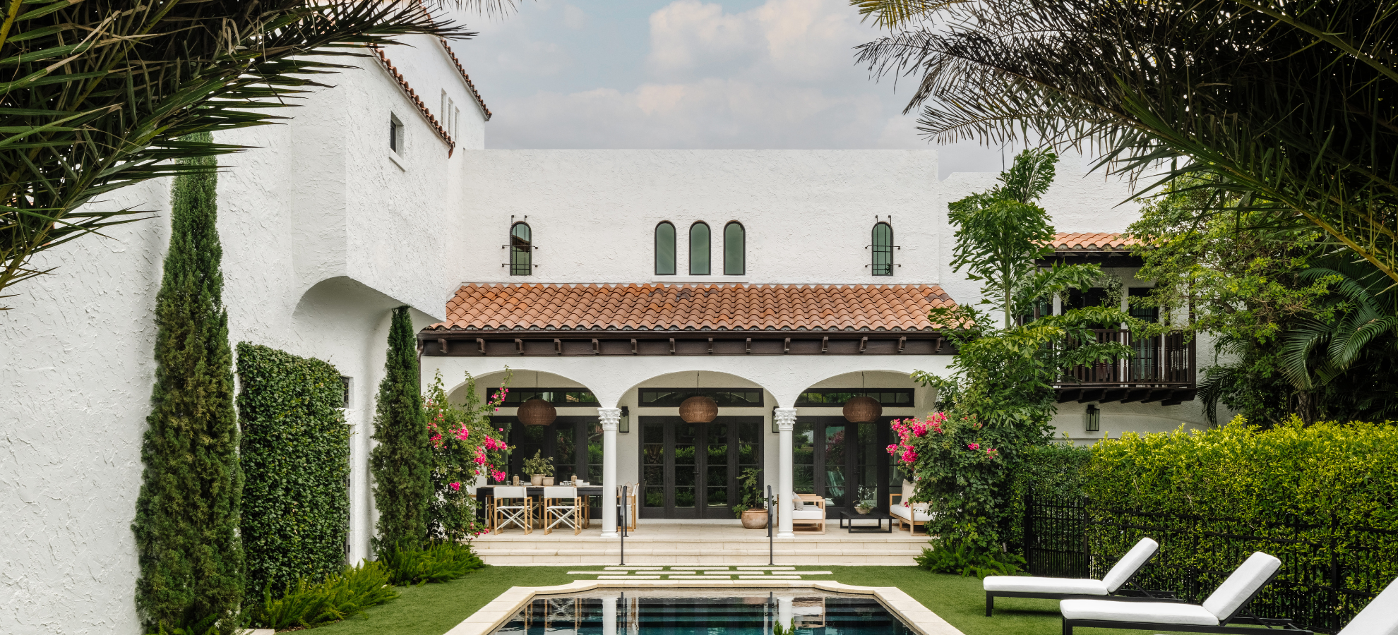 Spanish-style white villa with red tile roof, pool, and lush garden, a Calimia Home project in Coral Gables