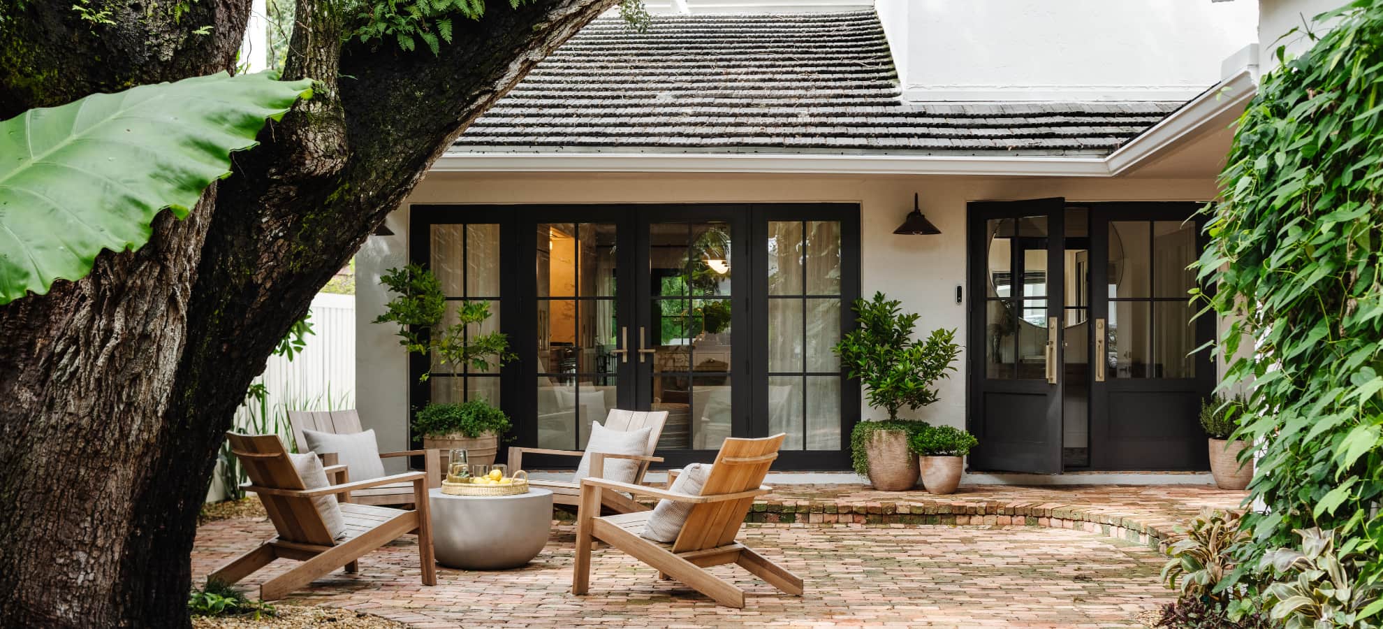 Exterior courtyard with teak lounge chairs, concrete fire table, brick terrace, and black-framed French doors designed by Calimia Home, luxury interior designers in Miami.