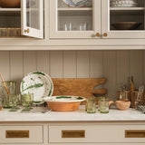 Calimia Home hand-blown olive recycled glass pitcher with etched thistle design displayed on a kitchen counter.