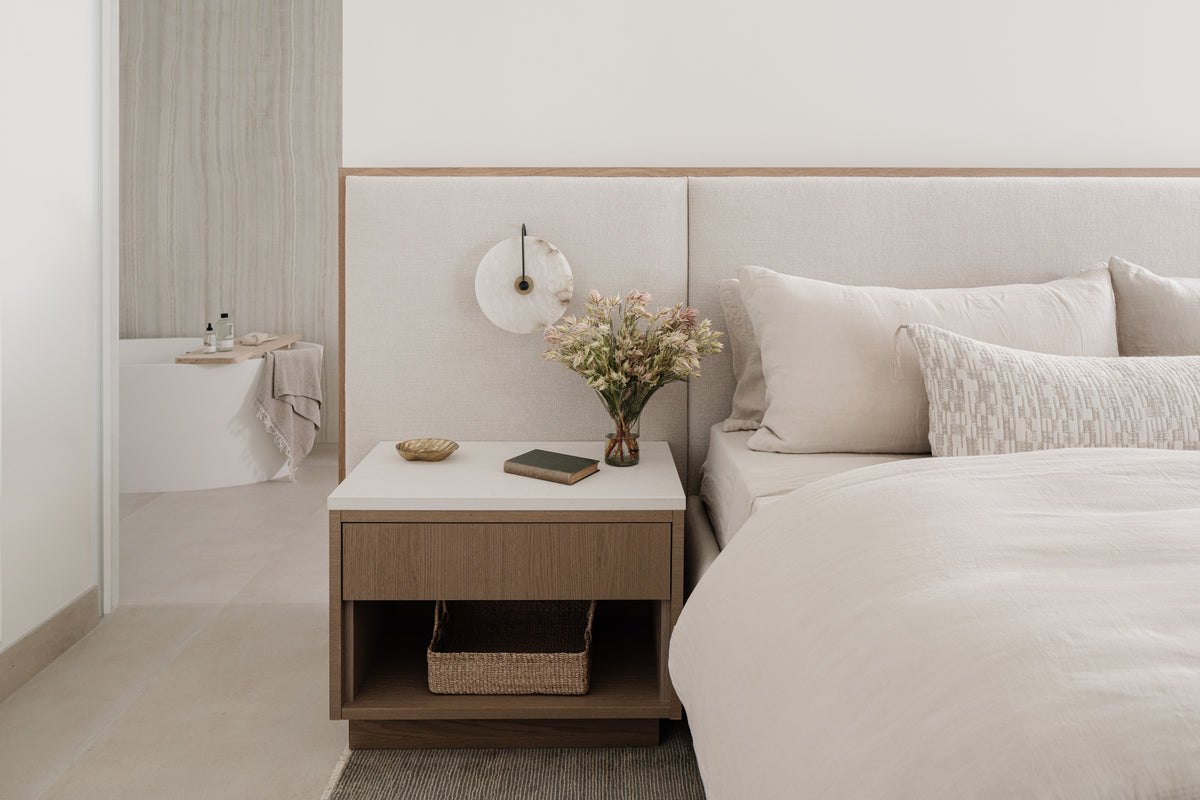 Bedroom detail with white oak nightstand, layered neutral bedding, and fresh blooms designed by Calimia Home