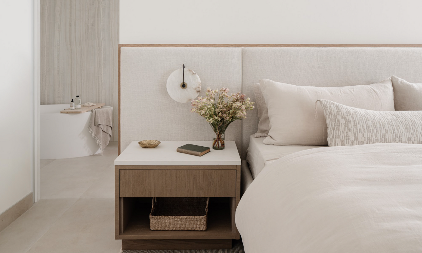 Bedroom detail with white oak nightstand, layered neutral bedding, and fresh blooms designed by Calimia Home