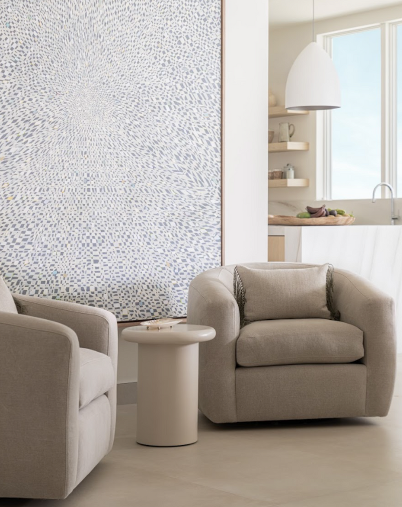 Pair of boucle swivel chairs beside a textured white canvas and sculptural side table
