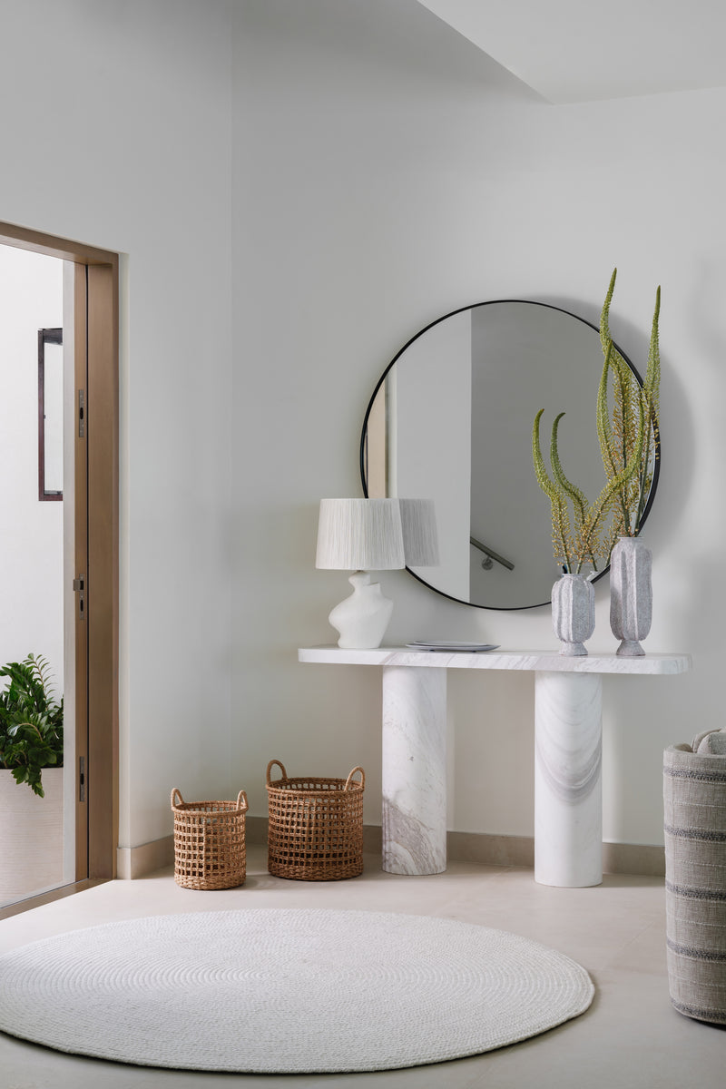 Entry vignette with round mirror, sculptural white console, ceramic vases, and woven baskets