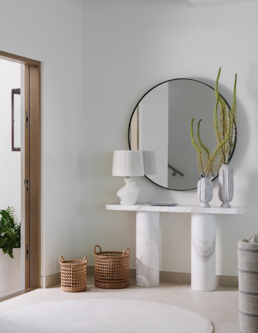 Entry vignette with round mirror, sculptural white console, ceramic vases, and woven baskets