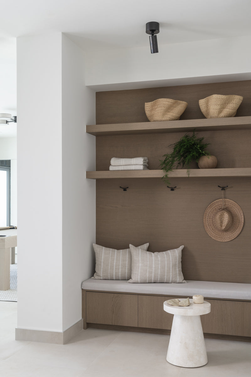Built-in mudroom bench with striped pillows, oak shelves, woven baskets, and a sun hat