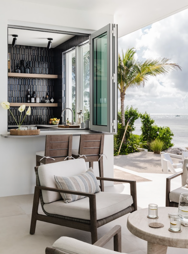 Outdoor bar with pass-through window and teak lounge seating by the sea at Peaceful Waters, Islamorada