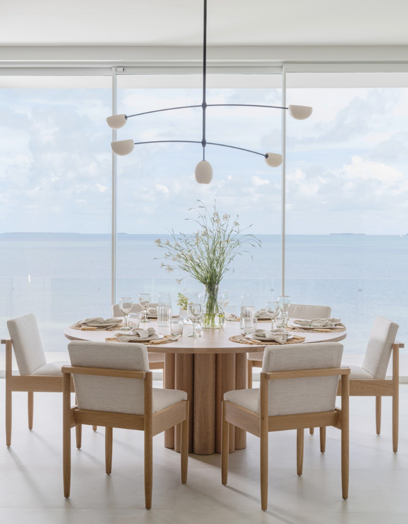 Round pedestal dining table set with glassware and linen chairs overlooking calm Florida Keys water