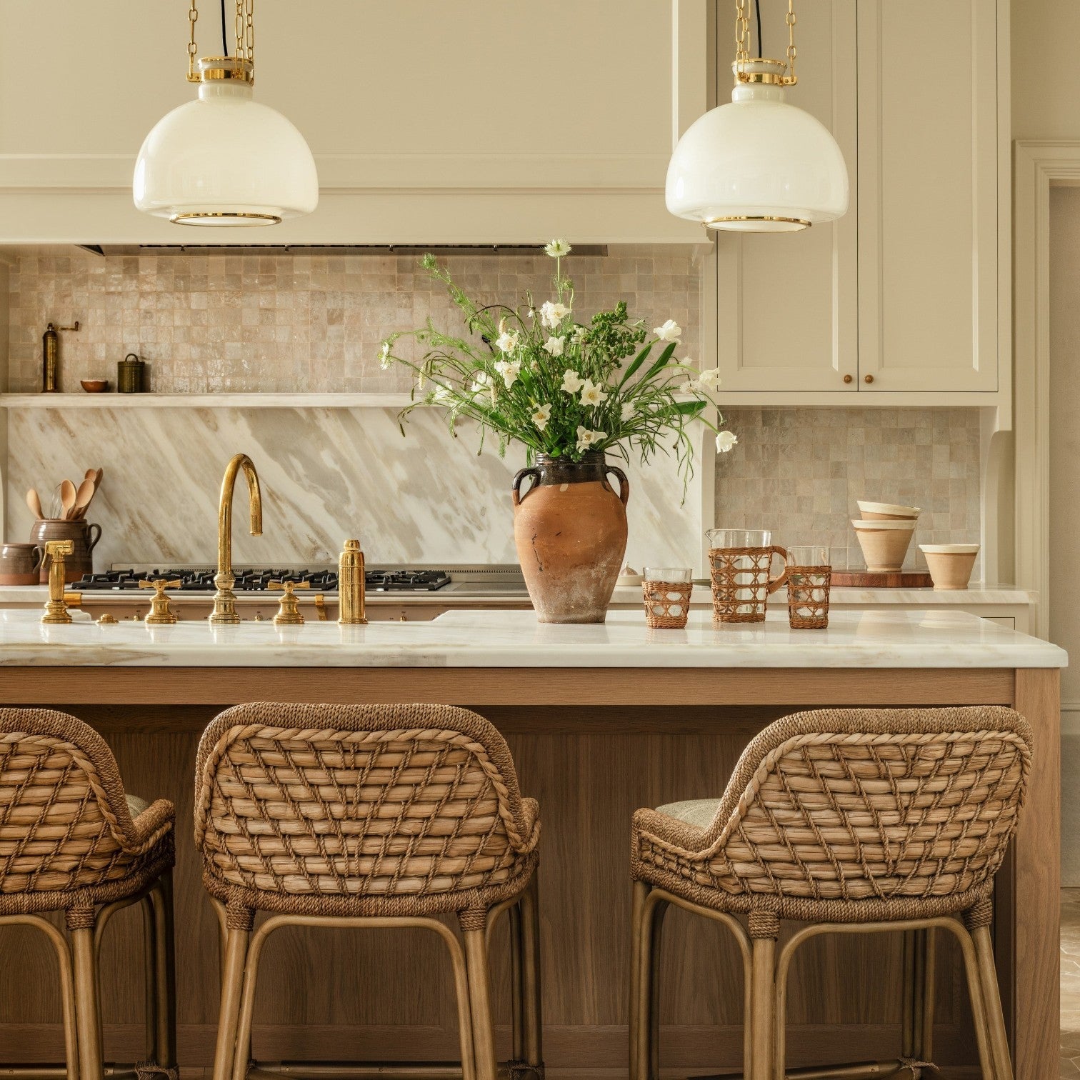 Calimia Home short glass pitcher with a woven rattan cage handle and matching tumblers on a marble kitchen island.