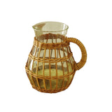 Calimia Home clear glass pitcher wrapped in handwoven natural seagrass with a sturdy handle on a linen tablecloth