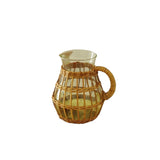 Calimia Home short glass pitcher wrapped in handwoven natural seagrass with a sturdy handle on a linen table