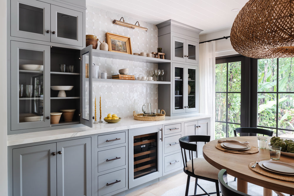 Gray-blue bar cabinets with glass fronts and wine fridge beside the breakfast table, designed by Calimia Home