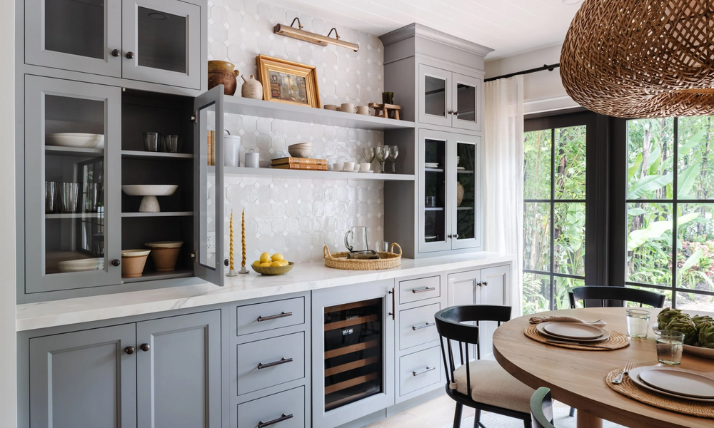 Gray-blue bar cabinets with glass fronts and wine fridge beside the breakfast table, designed by Calimia Home