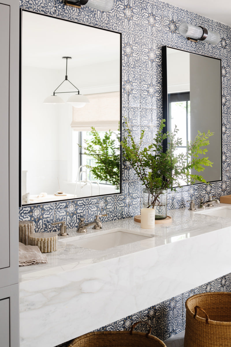 Bathroom with blue patterned tile wall, marble counter, and black-framed mirrors in this historic Miami renovation