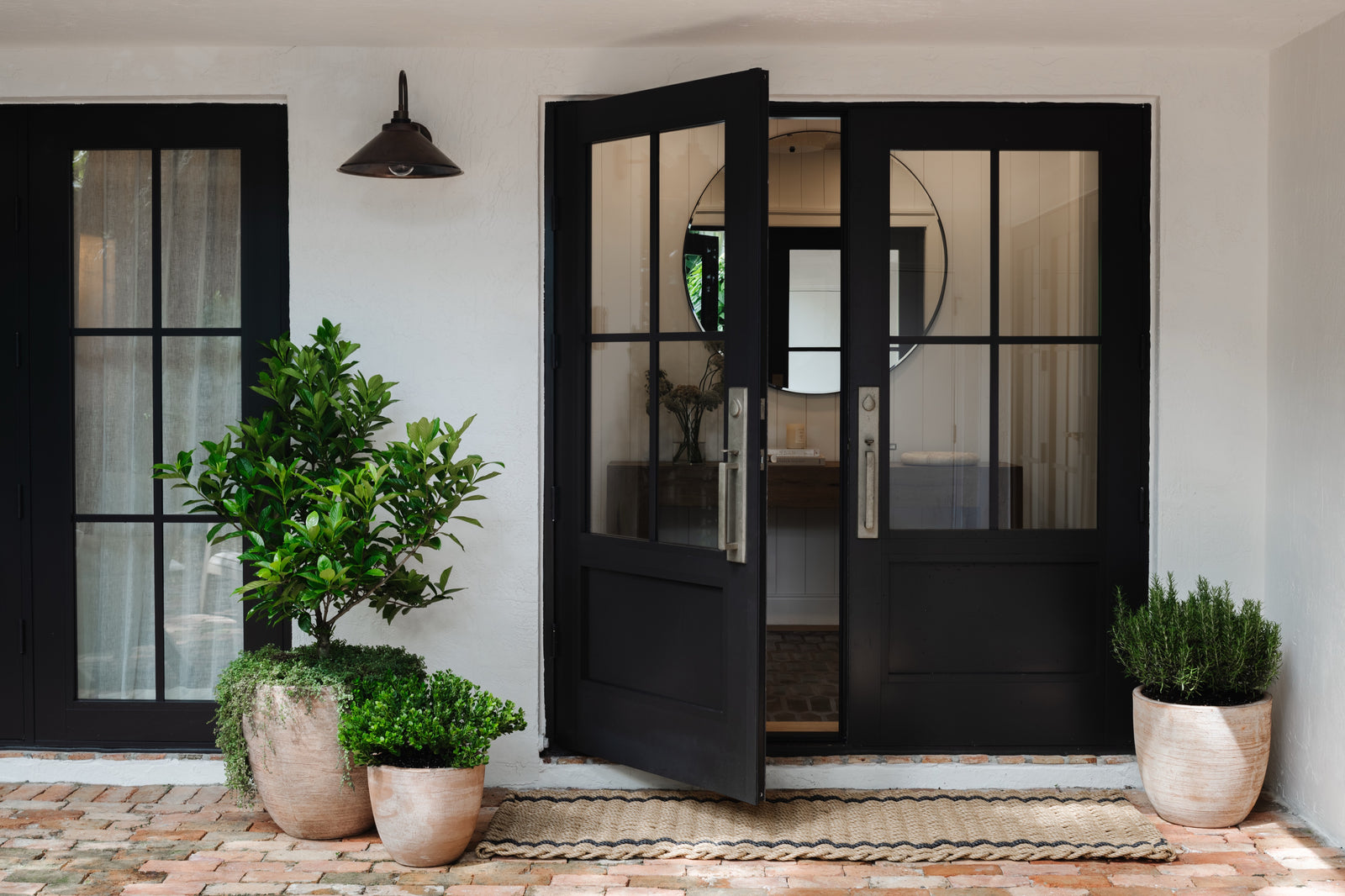 Black steel entry doors with potted citrus trees and terracotta planters at a historic Miami home