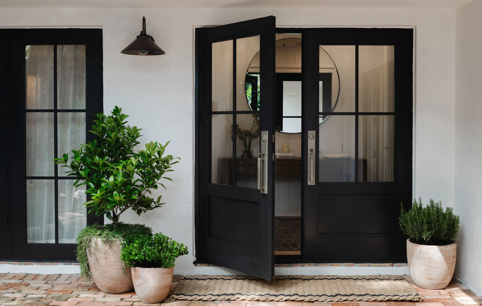 Black steel entry doors with potted citrus trees and terracotta planters at a historic Miami home
