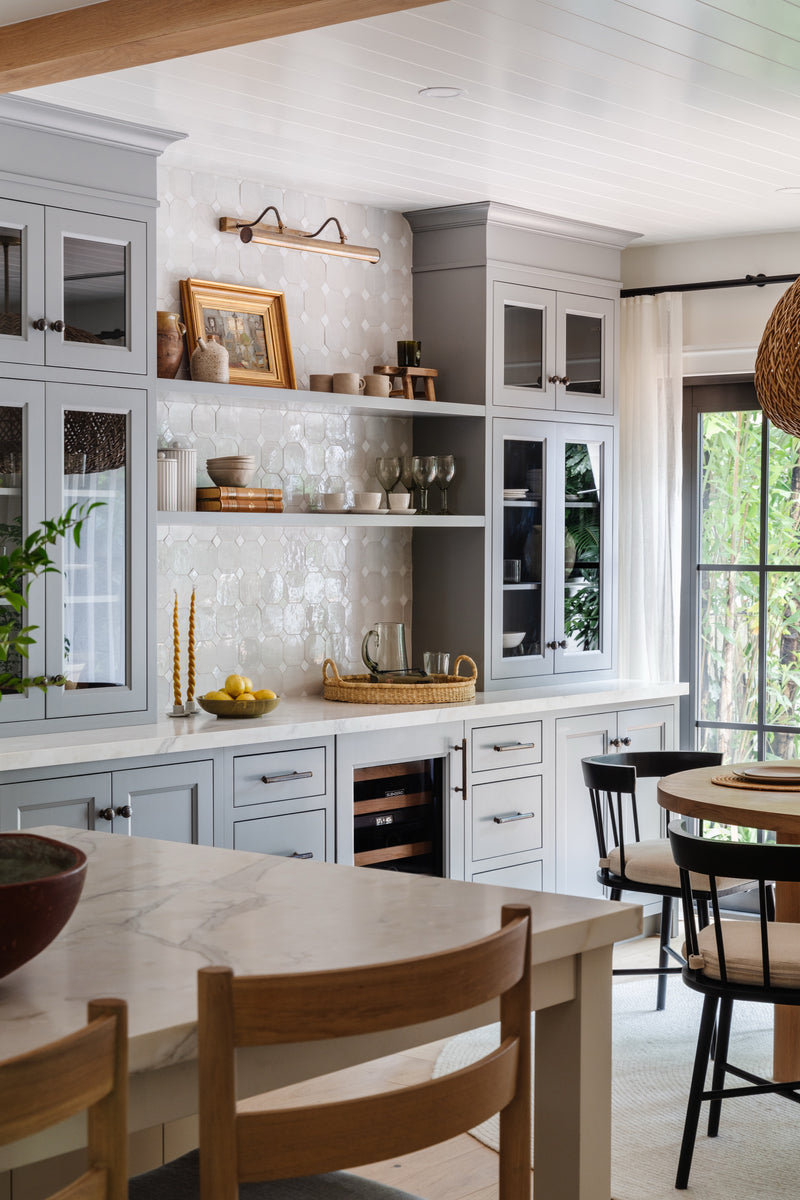 Breakfast corner with gray glass-front cabinets, patterned tile backsplash, and brass picture light