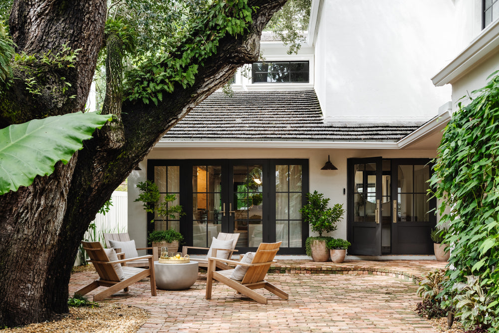 Brick courtyard with teak lounge chairs beneath a sprawling oak at the Raynolds Residence in Coconut Grove