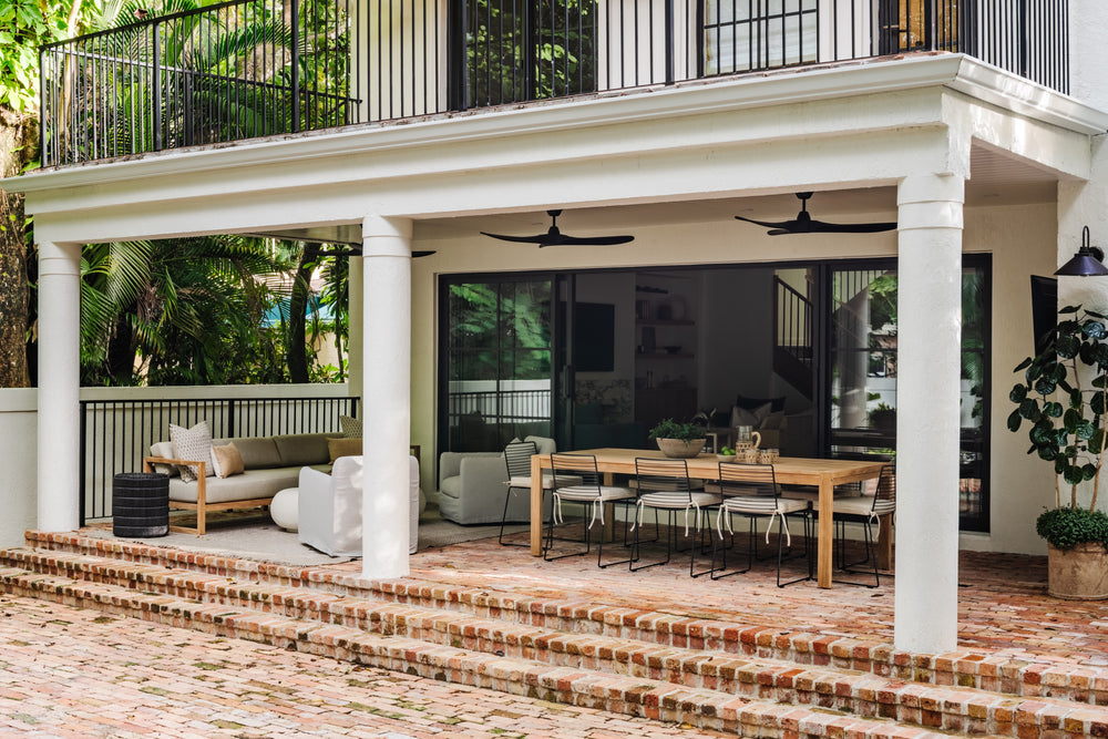 Covered outdoor dining porch with ceiling fans and brick steps beneath an upper balcony