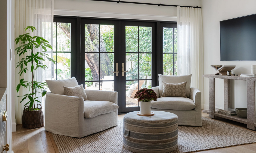 Bright den with linen swivel chairs, jute rug, and curtained French doors in the Raynolds Residence