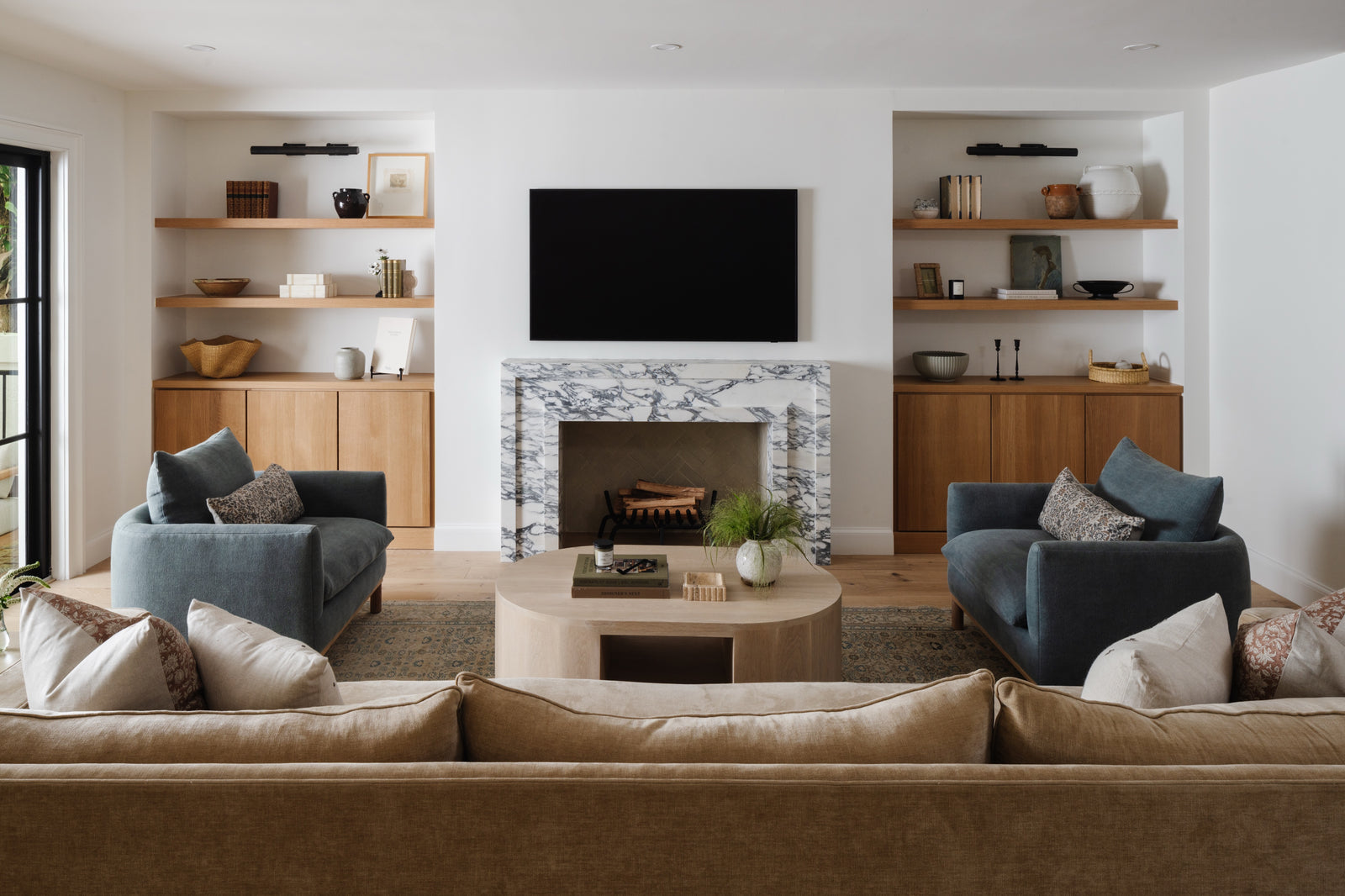 Family room with marble fireplace, built-in oak shelving, and a pair of navy armchairs