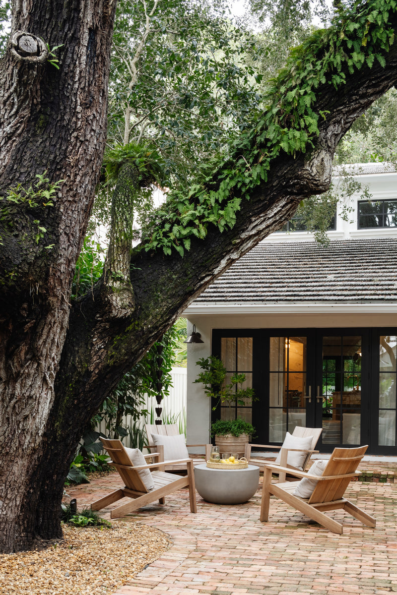 Teak lounge chairs around a concrete fire bowl beneath a historic oak at the Raynolds Residence