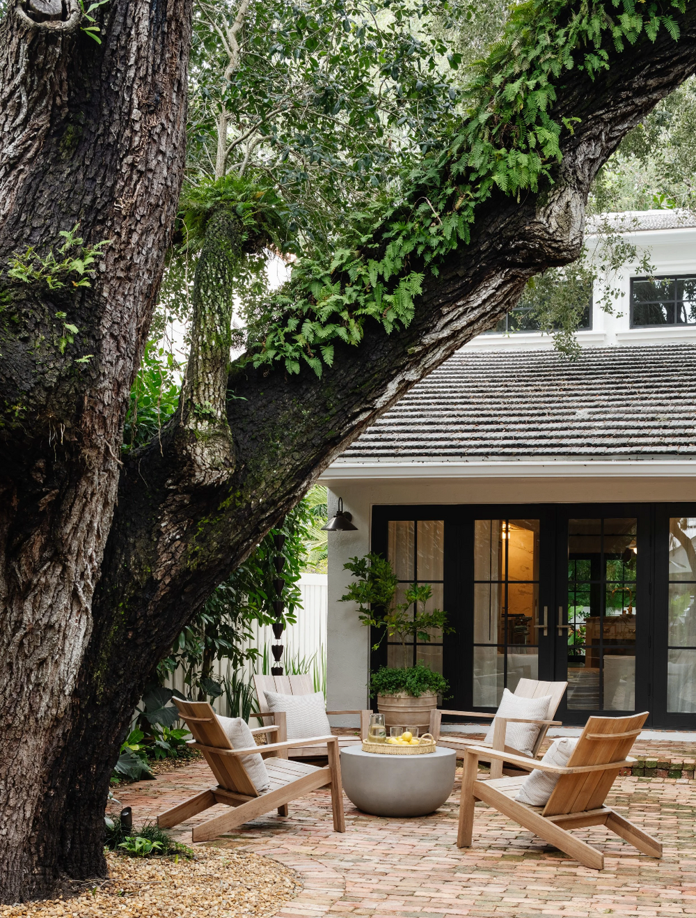 Teak lounge chairs around a concrete fire bowl beneath a historic oak at the Raynolds Residence