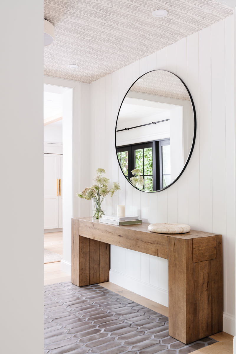 Hallway with round black mirror, chunky wood console table, and vertical shiplap paneling
