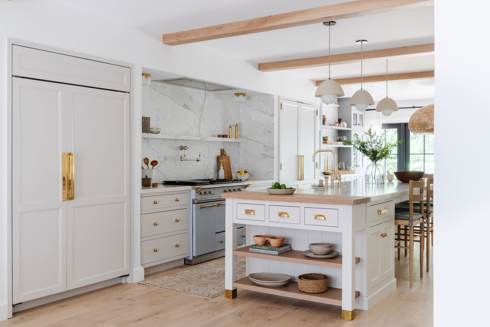 Light-filled kitchen with paneled refrigerator, oak ceiling beams, and freestanding marble-top island