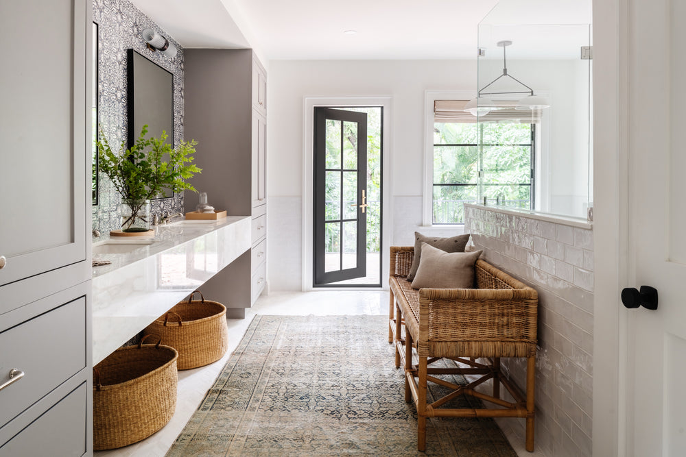 Primary bath with long white vanity, rattan bench, and vintage runner designed by Calimia Home