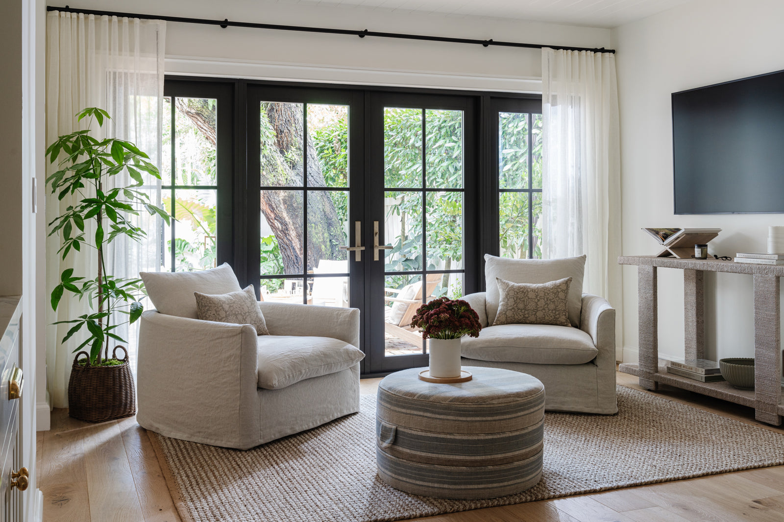 Sitting room with white swivel chairs, round stone coffee table, and black French doors designed by Calimia Home