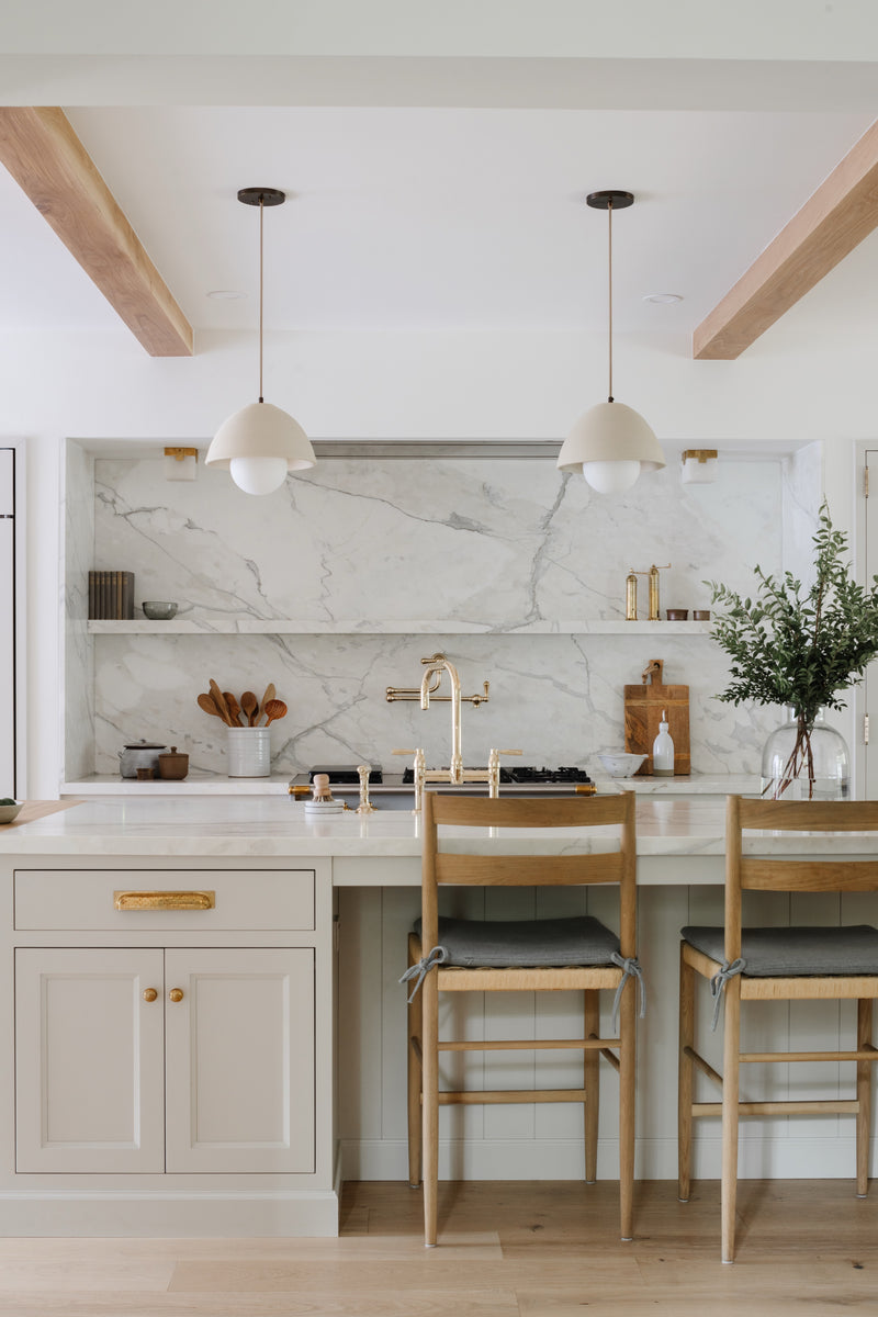 White kitchen with marble slab backsplash, dome pendants, and oak counter stools in the Raynolds Residence